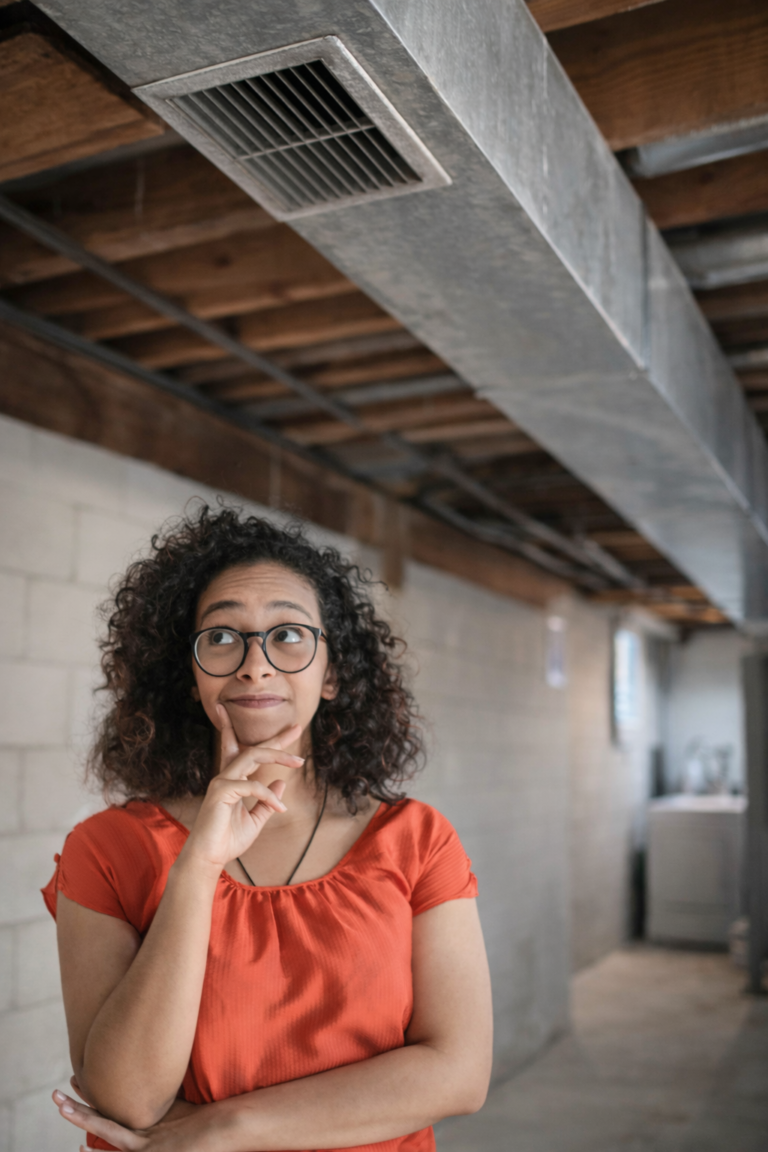 woman in abasement looking up at dirty air ducts