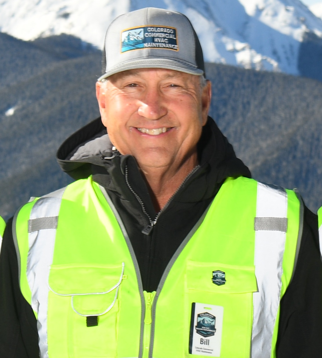 HVAC technician wearing a yellow vest with mountain background.